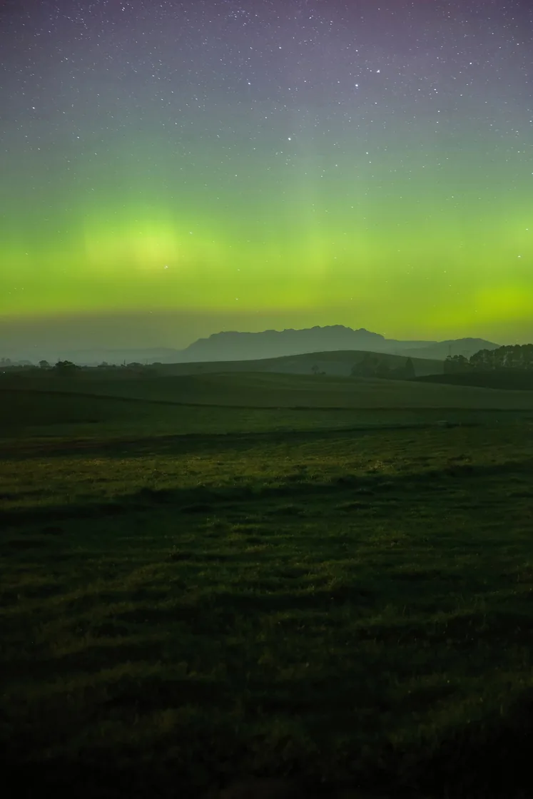 Green aurora lighting the sky above rolling Tasmanian hills